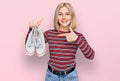 Young blonde woman holding white casual shoes smiling happy pointing with hand and finger Royalty Free Stock Photo