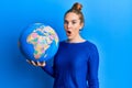 Young blonde woman holding world ball scared and amazed with open mouth for surprise, disbelief face Royalty Free Stock Photo