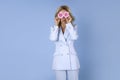 Young blonde woman holds pink gerbera daisy flower, covers eyes, dressed in fashionable blue, poses on blue background. Spring Royalty Free Stock Photo