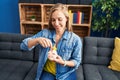 Young blonde woman inserting coin on piggy bank sitting on sofa at home Royalty Free Stock Photo