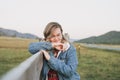 Young blonde woman in jeans jacket and red dress near old wooden fence on the mountains background Royalty Free Stock Photo