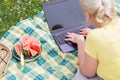 blonde woman with a laptop lies on a blanket in the green grass on a sunny day Royalty Free Stock Photo