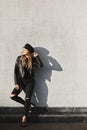Young blonde woman in a leather jacket and ripped jeans enjoying the sun outdoors against the urban wall. Sexy model Royalty Free Stock Photo