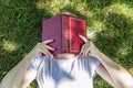 A young blonde woman lies in a park on the grass with her face covered in a book. Summer sunny day. Top view. Relaxation in nature Royalty Free Stock Photo