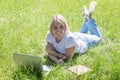 A young blonde woman lies in a park on the grass with a laptop. Blogging, education and remote work