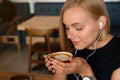 Young blonde woman listening podcast while drinking coffee at the coffe shop Royalty Free Stock Photo