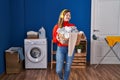 Young blonde woman listening to music holding basket with clothes at laundry room Royalty Free Stock Photo