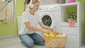 Young blonde woman listening to music holding clothes of basket at laundry room Royalty Free Stock Photo