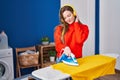 Young blonde woman listening to music ironing clothes at laundry room Royalty Free Stock Photo