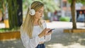 Young blonde woman listening to music with serious face at park Royalty Free Stock Photo