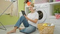 Young blonde woman listening to music sitting on floor at laundry room Royalty Free Stock Photo