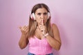 Young blonde woman listening to music using headphones asking to be quiet with finger on lips pointing with hand to the side Royalty Free Stock Photo