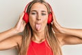 Young blonde woman listening to music using headphones sticking tongue out happy with funny expression Royalty Free Stock Photo
