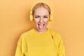 Young blonde woman listening to music using headphones sticking tongue out happy with funny expression Royalty Free Stock Photo