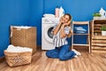 Young blonde woman listening to music waiting for washing machine at laundry room Royalty Free Stock Photo