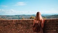 A young blonde woman is looking at the view beyond a brick wall Corinaldo, Marche, Italy