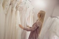 Young blonde woman looks different dress on the hanger. Bridal shop. Royalty Free Stock Photo