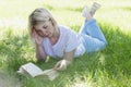 A young blonde woman is lying on the grass in a park on a sunny summer day and is reading a book. Recreation and distance learning Royalty Free Stock Photo