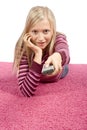 Young blonde woman lying on the pink carpet with remote control Royalty Free Stock Photo