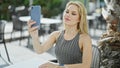 Young blonde woman making selfie by the smartphone sitting on table at coffee shop terrace Royalty Free Stock Photo