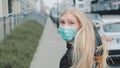 Young blonde woman in a medical mask escaping from somebody on the street.