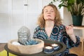 Young blonde woman meditating at home with candle lights and incense stick on foreground