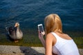 Young blonde woman with mobile phone, photographing birds on the lake in London Hyde Park