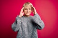 Young blonde woman with modern short hair wearing casual sweater over pink background with hand on headache because stress