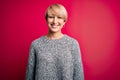 Young blonde woman with modern short hair wearing casual sweater over pink background with a happy and cool smile on face