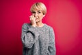 Young blonde woman with modern short hair wearing casual sweater over pink background looking stressed and nervous with hands on Royalty Free Stock Photo