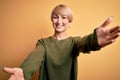 Young blonde woman with modern short hair wearing casual sweater over yellow background looking at the camera smiling with open Royalty Free Stock Photo