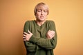 Young blonde woman with modern short hair wearing casual sweater over yellow background shaking and freezing for winter cold with Royalty Free Stock Photo