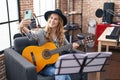 Young blonde woman musician making selfie by smartphone holding classical guitar at music studio