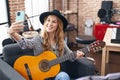 Young blonde woman musician making selfie by smartphone holding classical guitar at music studio