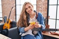 Young blonde woman musician playing electrical guitar using smartphone at music studio Royalty Free Stock Photo