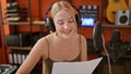 Young blonde woman musician reading music sheet singing song at music studio