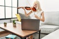 Young blonde woman musician smiling confident having online violin lesson at home