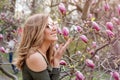 Young blonde woman near blossoming magnolia flowers tree in spring park on sunny day. Magnolia trees. Beautiful happy Royalty Free Stock Photo