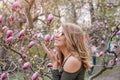 Young blonde woman near blossoming magnolia flowers tree in spring park on sunny day. Magnolia trees. Beautiful happy Royalty Free Stock Photo