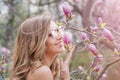 Young blonde woman near blossoming magnolia flowers tree in spring park on sunny day. Magnolia trees. Beautiful happy Royalty Free Stock Photo