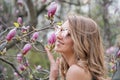 Young blonde woman near blossoming magnolia flowers tree in spring park on sunny day. Magnolia trees. Beautiful happy Royalty Free Stock Photo