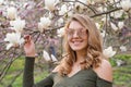 Young blonde woman near blossoming magnolia flowers tree in spring park on sunny day. Magnolia trees. Beautiful happy Royalty Free Stock Photo