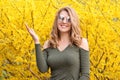 Young blonde woman near blossoming yellow trees in spring park on sunny day. Beautiful happy girl enjoying smell in a Royalty Free Stock Photo