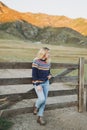 Young blonde woman in nordic sweater and jeans near old wooden fence on the mountains background Royalty Free Stock Photo