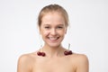 Young blonde woman with perfect skin holds a cherry on her clavicles. Royalty Free Stock Photo