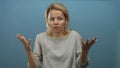 Young blonde woman performs a casual shrug gesture with both bare palms raised in a soft blue studio setting; confusion Royalty Free Stock Photo