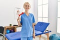 Young blonde woman physiotherapist smiling confident holding diploma at rehab clinic