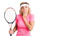 Young blonde woman playing tennis holding racket covering mouth with hand, shocked and afraid for mistake