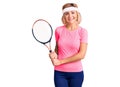 Young blonde woman playing tennis holding racket looking positive and happy standing and smiling with a confident smile showing Royalty Free Stock Photo