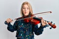 Young blonde woman playing violin making fish face with mouth and squinting eyes, crazy and comical